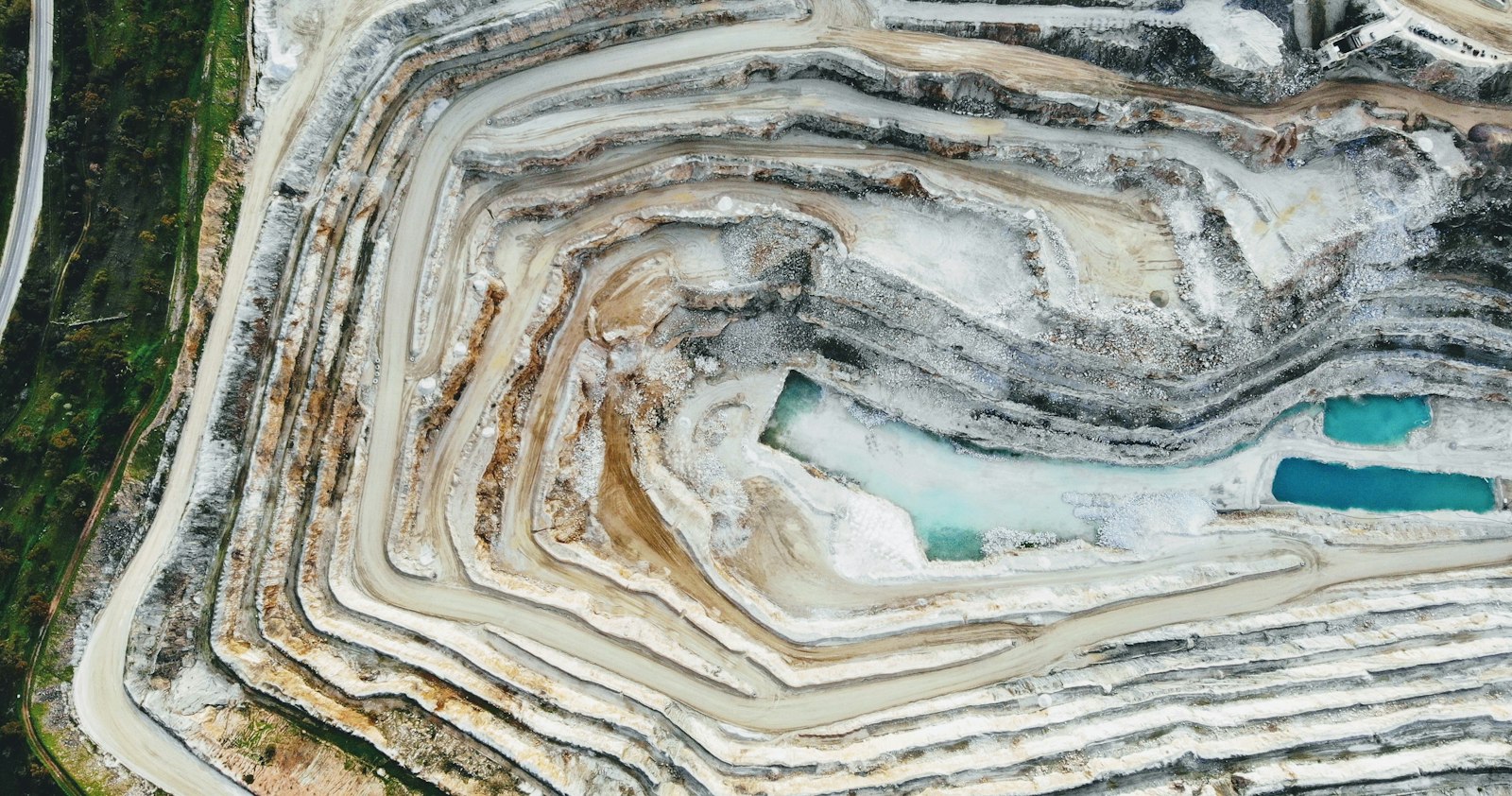 An open pit mine from above, with blue water pooled on its benches