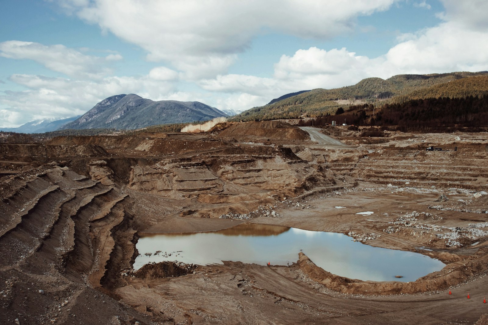 An open pit with water pooled at its base, below brown terraced slopes